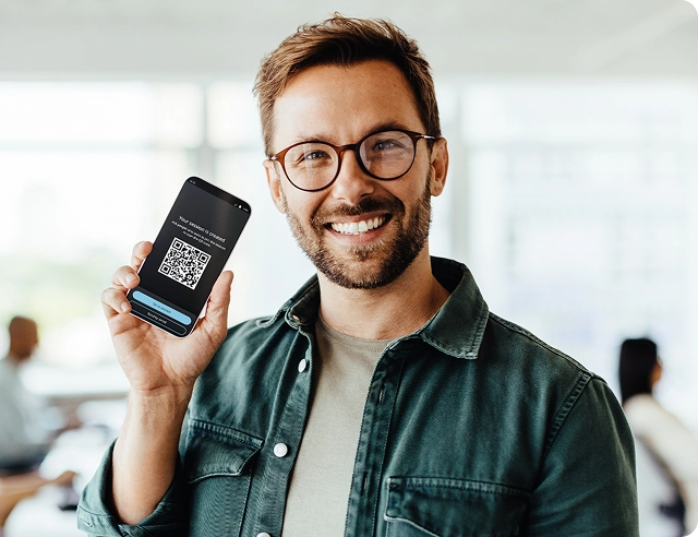 Un homme souriant tenant un smartphone affichant un code QR pour rejoindre Vasco Audience.