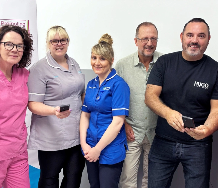 Cinq personnes souriantes se tiennent ensemble en tenue de soins de santé, deux d’entre elles tenant un appareil de traduction.