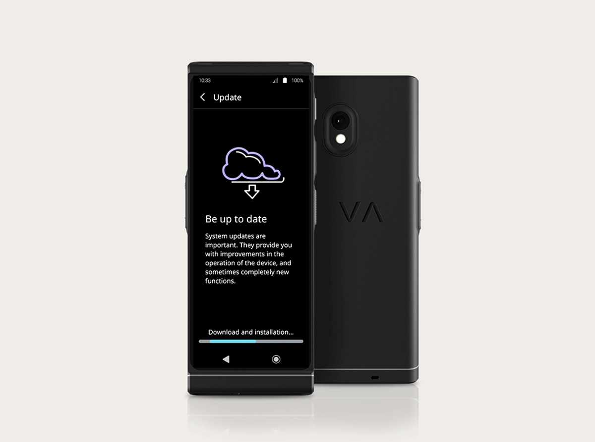 Une photo de produit prise en studio du Vasco Translator V4 montrant l'interface de mise à jour du système. Deux appareils noirs sont placés côte à côte : l'un tourné vers l'avant et l'autre montrant l'arrière. L'écran affiche une icône en forme de nuage avec une flèche de téléchargement, le titre « Restez à jour » et une barre de progression en bas intitulée « Téléchargement et installation... ». La vue arrière met en avant la double caméra et le logo « VA » en relief.