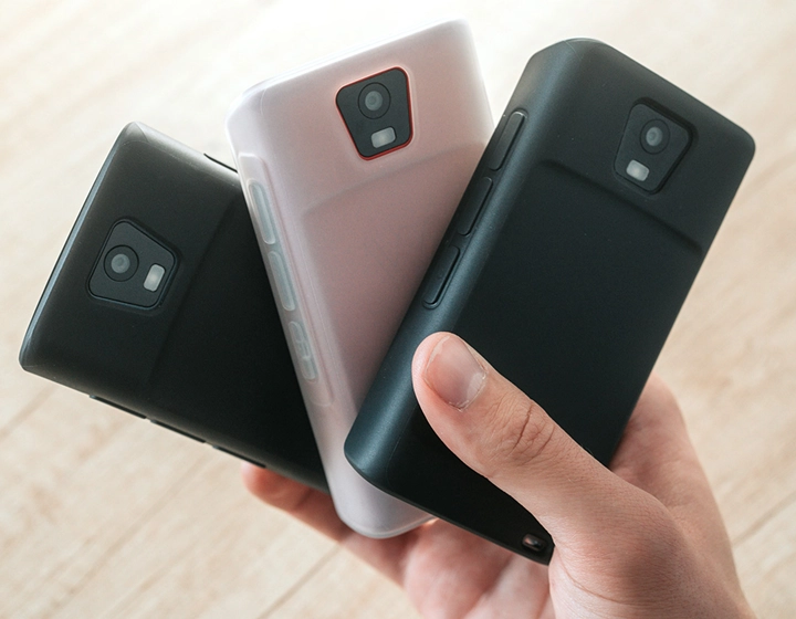 Personne tenant trois appareils Vasco Translator Q1 dans des coques en silicone, présentant trois couleurs différentes : Solid Black, Dark Caramel et Milky White.