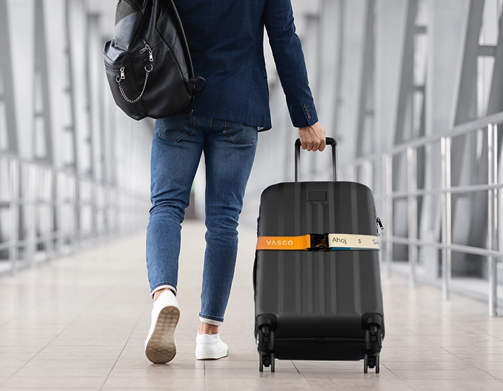 Une valise noire munie d'une sangle de sécurité Vasco aux couleurs de l'arc-en-ciel est tirée par un homme qui traverse un aéroport.